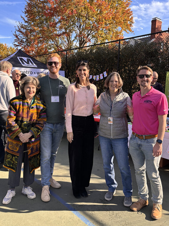 A group of adults stand shoulder to shoulder with a beautiful blue sky and golden autumn tree in the background