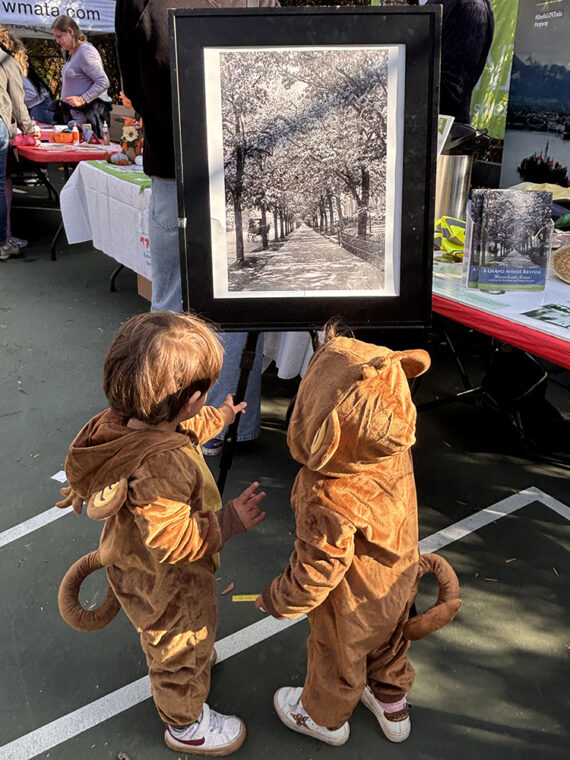 Two small children dressed in Halloween costumes study a photo of 1913 Embassy Row at the RMA information table.