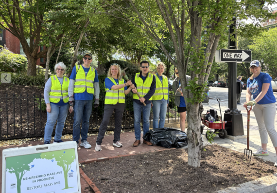 A group of smiling volunteers on shaded city sidewalk proudly display their treekeeping tools after working to help trees